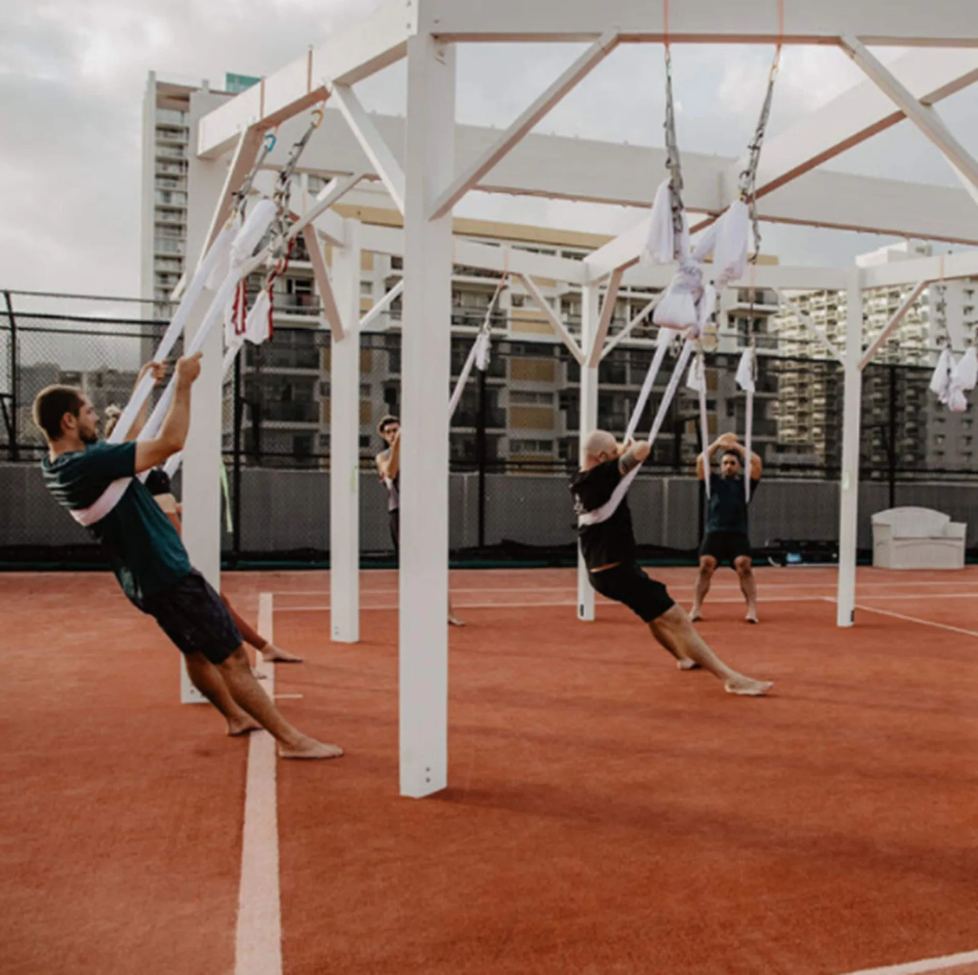 Guests using suspended fitness straps on an outdoor court at 'Alohilani Resort Waikiki Beach.