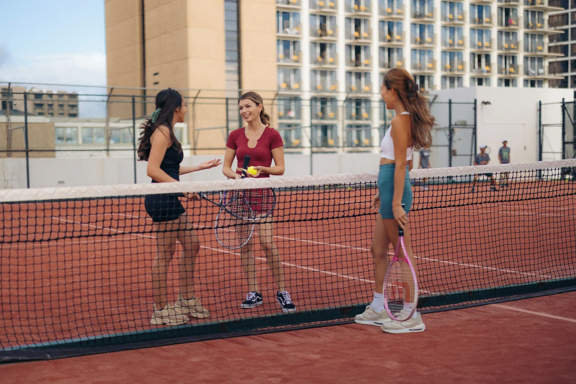 Three guests with tennis rackets on an outdoor court at 'Alohilani Resort Waikiki Beach.