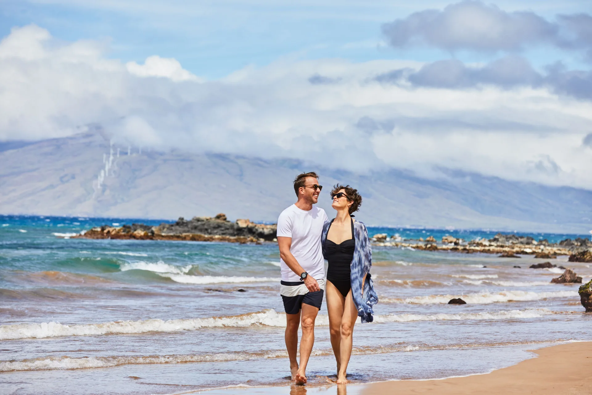 Couple walking on the beach with waves near Andaz Maui at Wailea Resort.