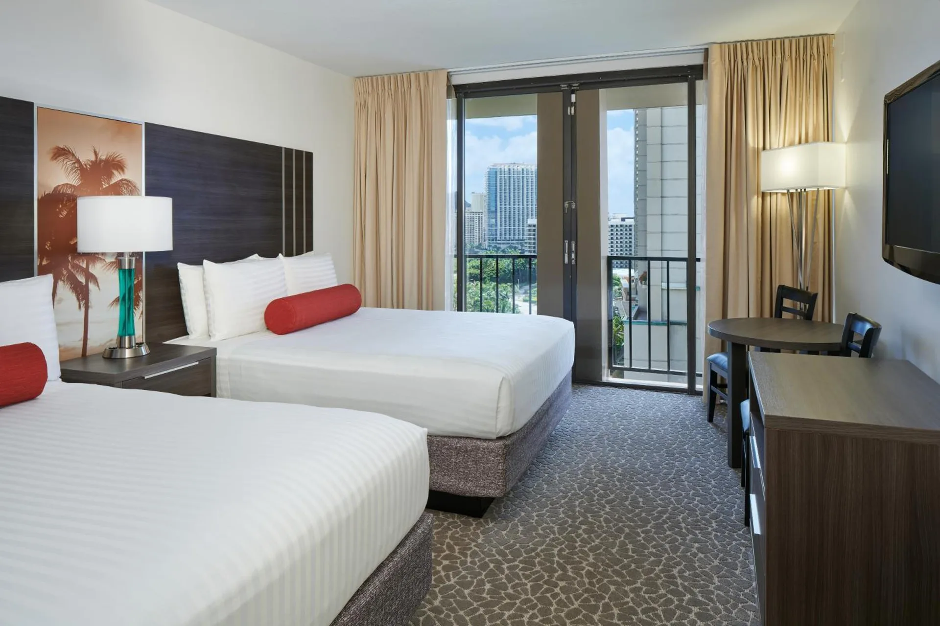 Two beds, balcony doors, table, and wall-mounted TV in a room at Aqua Palms Waikiki.