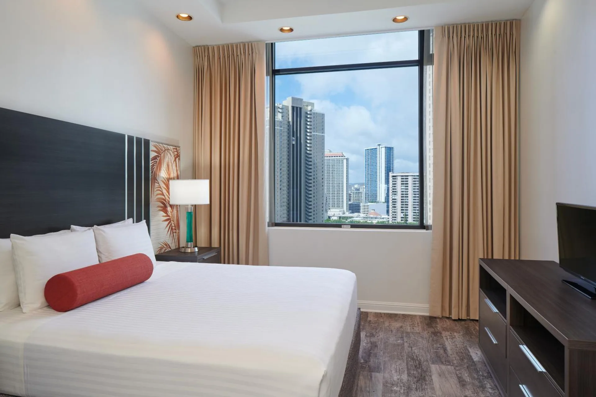 Guest room with king bed, TV, and city window view at Aqua Palms Waikiki.