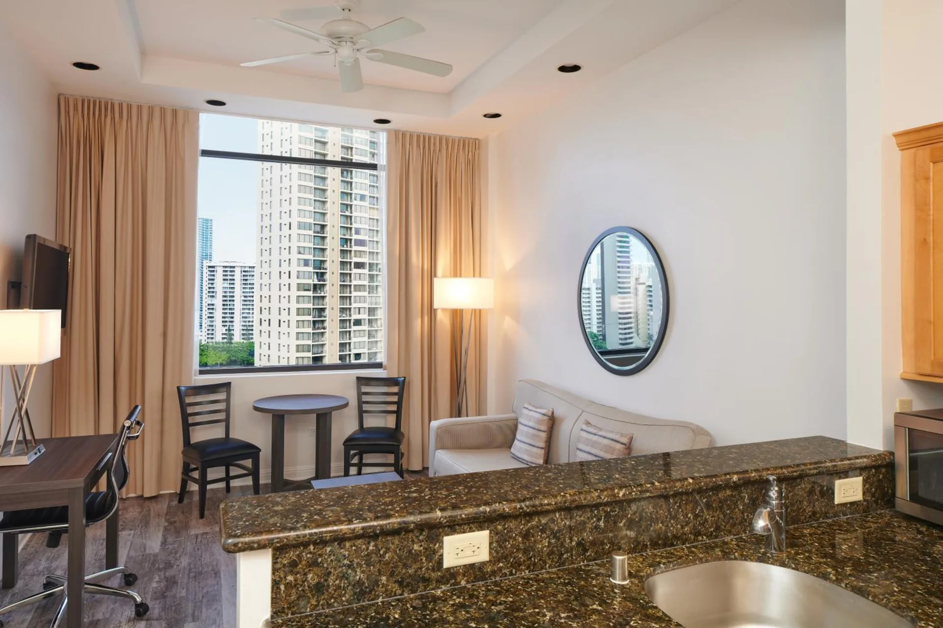 Guest room living area with kitchenette counter and city window at Aqua Palms Waikiki.