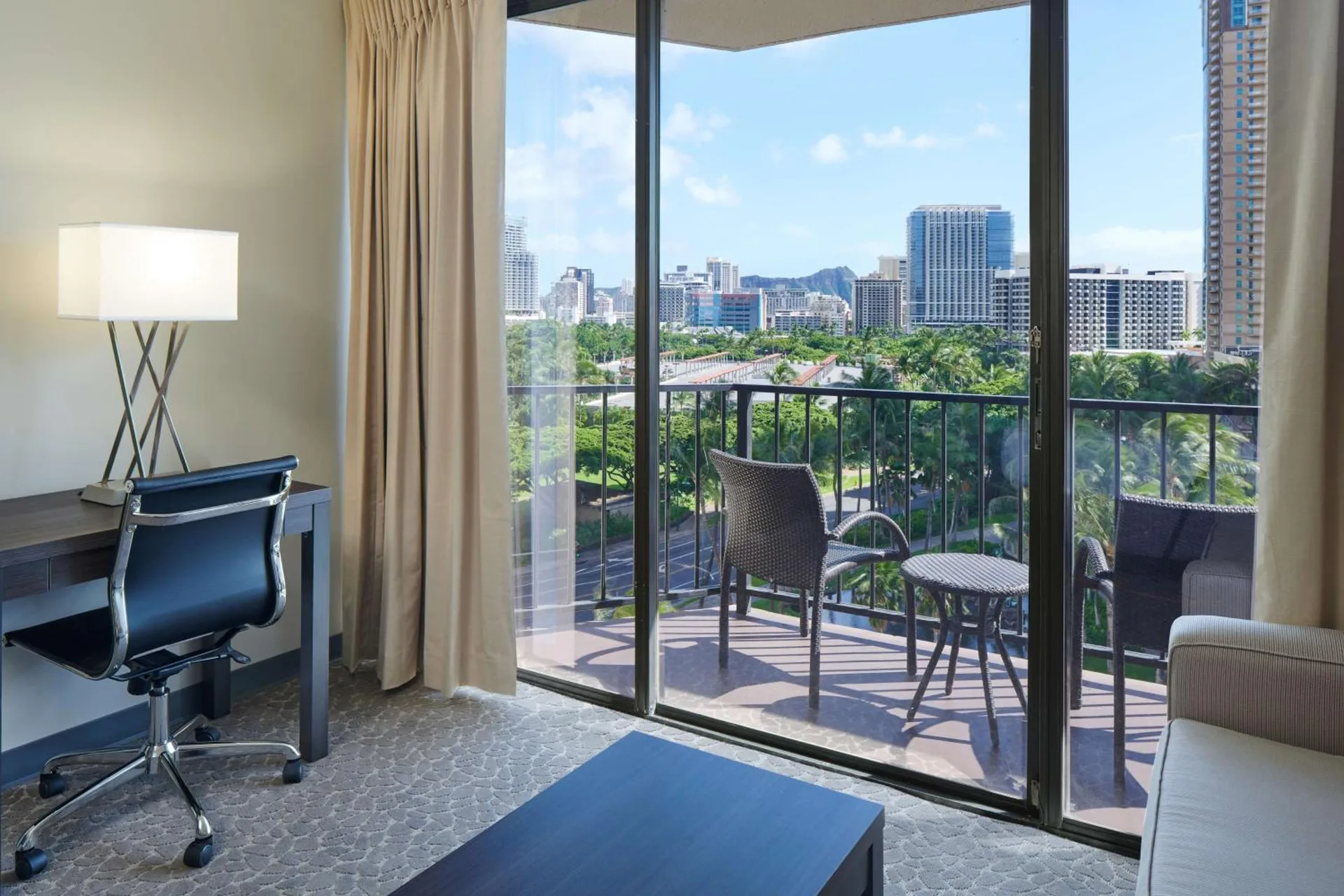 Guest room sitting area with desk and balcony view at Aqua Palms Waikiki.