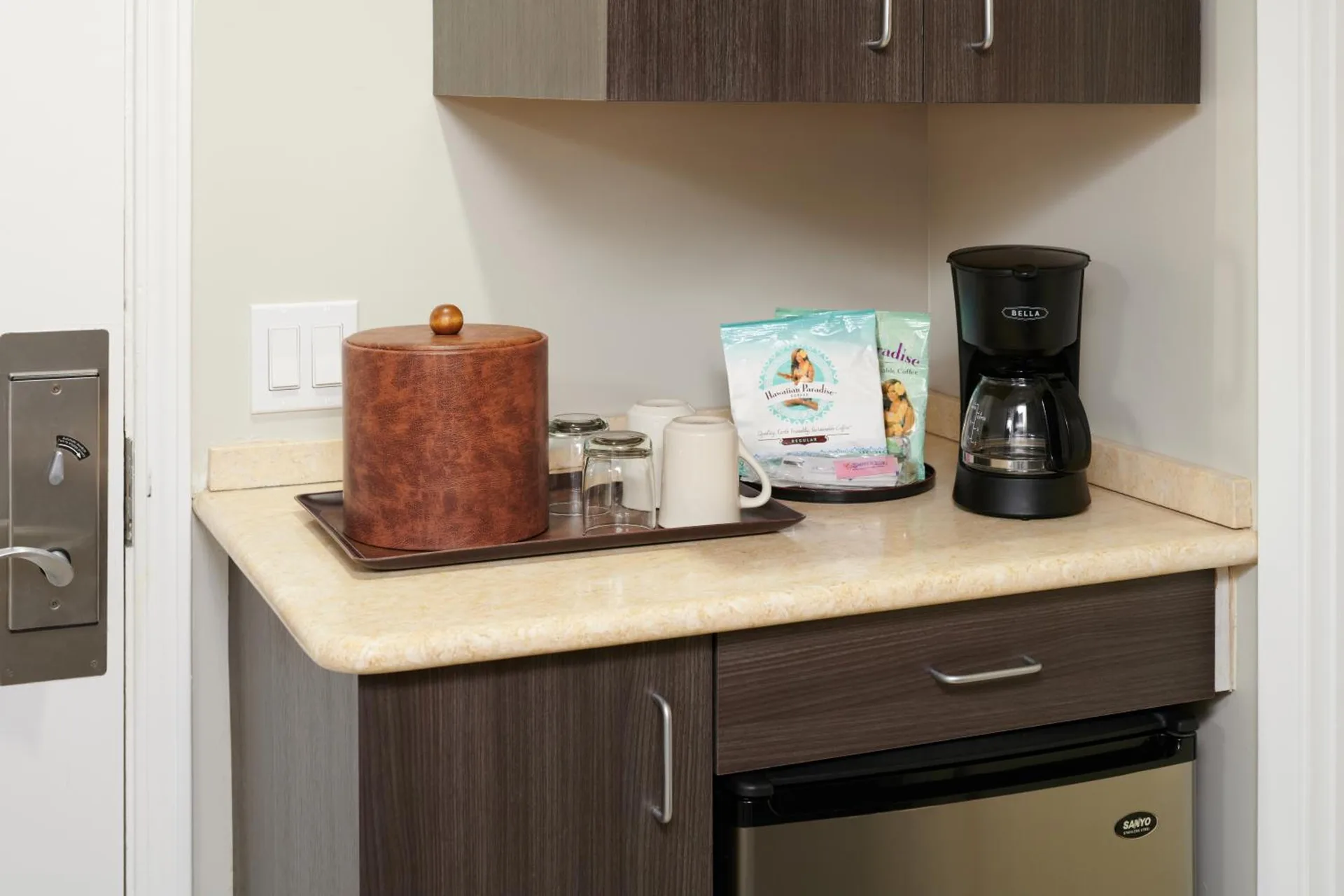 In-room coffee station with cups, cabinets, and mini fridge at Aqua Palms Waikiki.