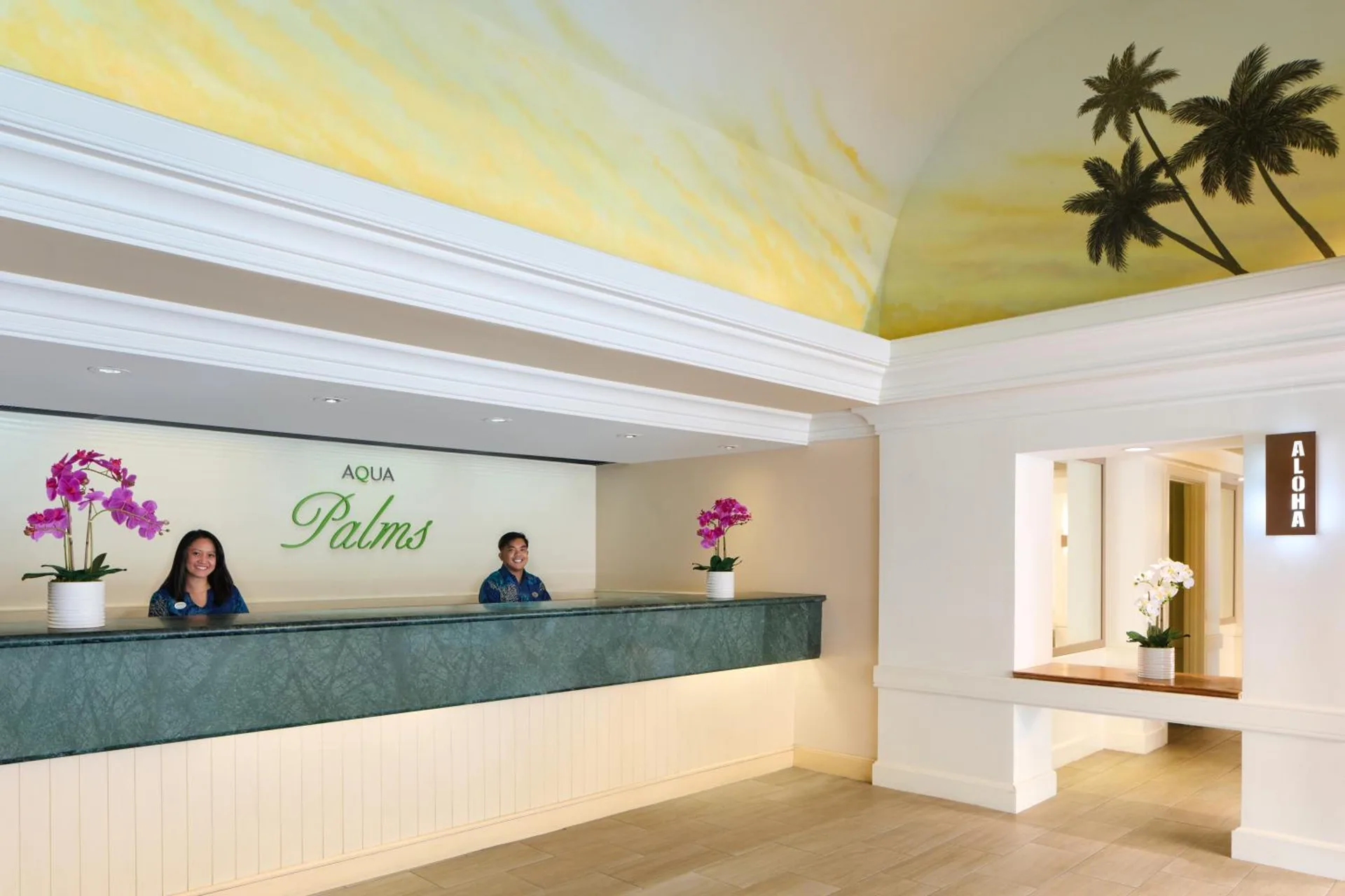 Front desk with staff, orchids, and palm mural in the lobby at Aqua Palms Waikiki.