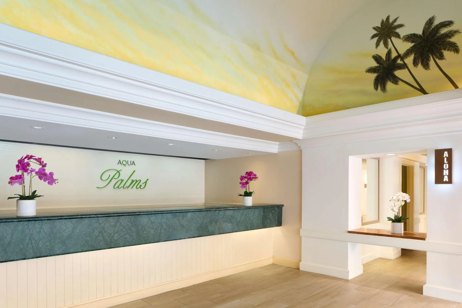 Front desk counter, orchids, and palm mural in the lobby at Aqua Palms Waikiki.