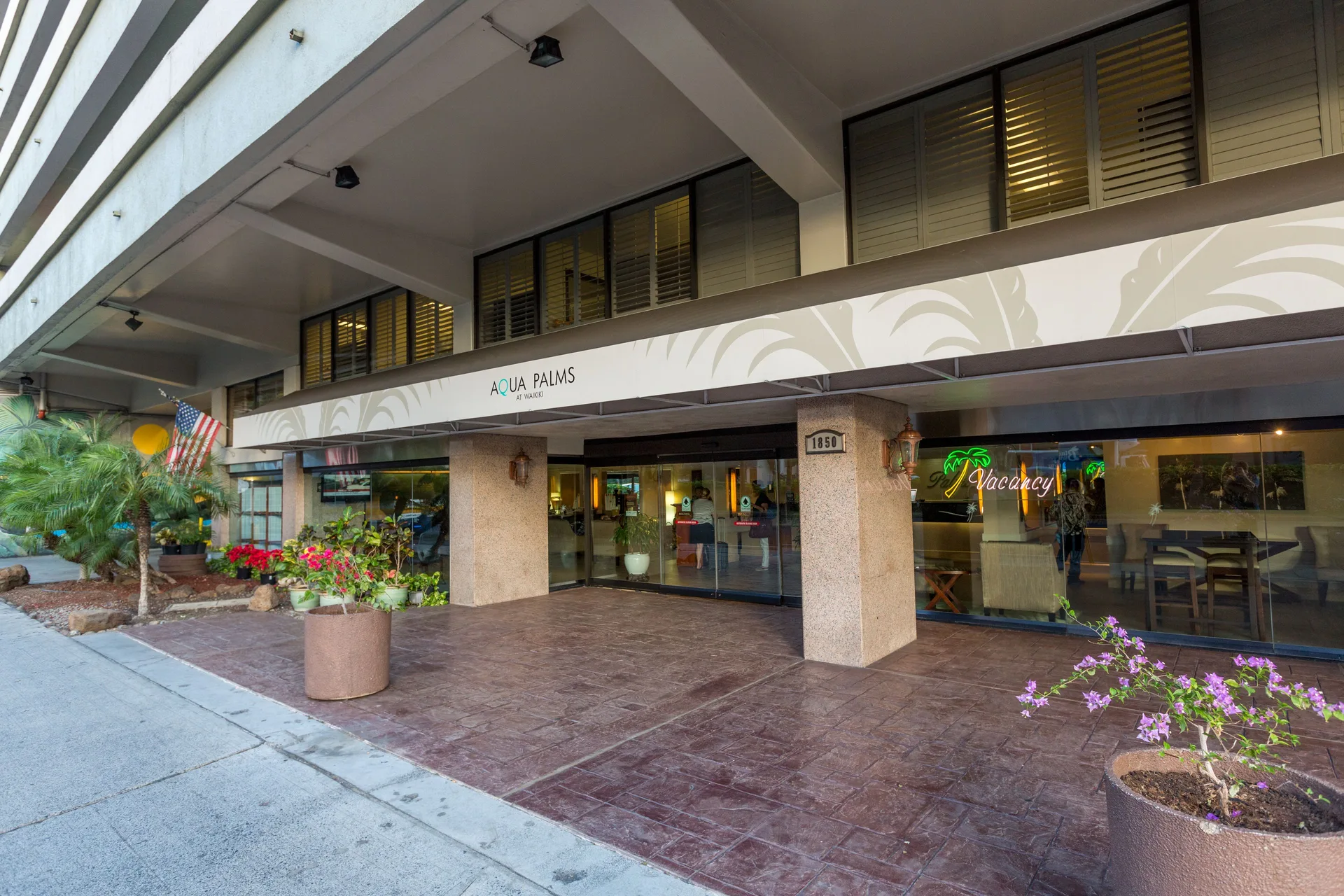 Covered main entrance with Aqua Palms Waikiki signage and sidewalk planters at Aqua Palms Waikiki.