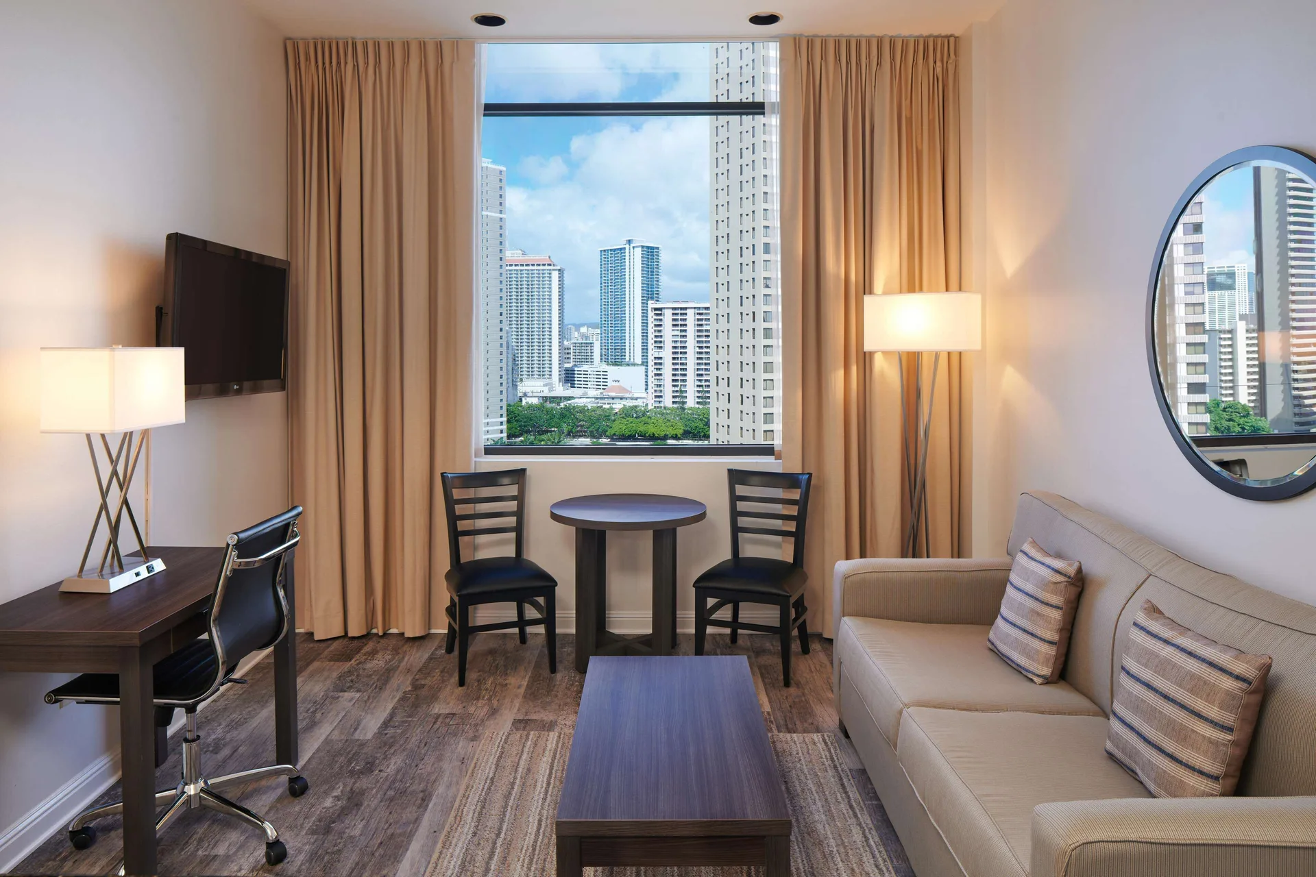 Luxury Suite living area with sofa, desk, dining table and city window at Aqua Palms Waikiki.