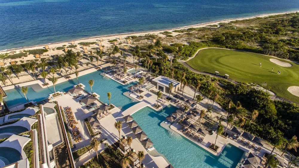 Aerial view of resort pools, beach, ocean, and golf green at Atelier Playa Mujeres.