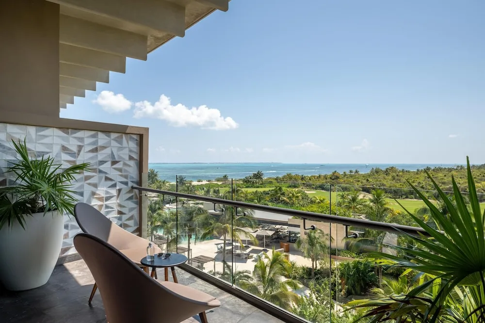 Balcony seating with ocean and golf-course views at Atelier Playa Mujeres.