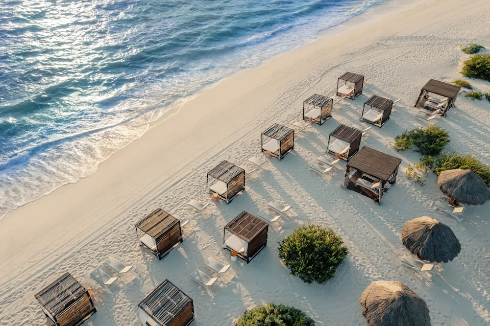 Beach cabanas and loungers line the sand beside the sea at Atelier Playa Mujeres.