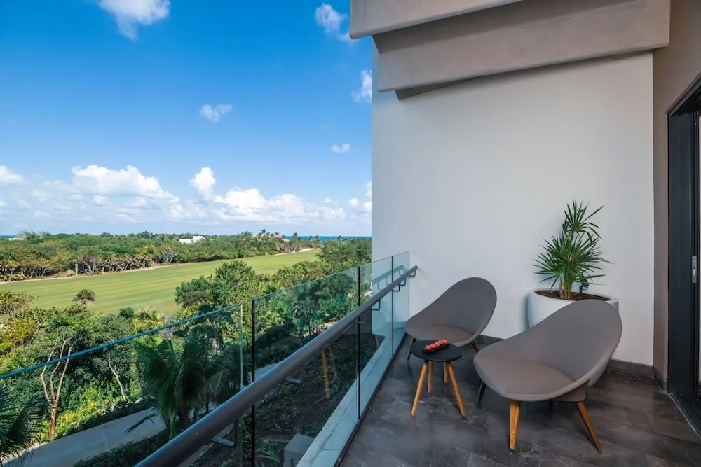 Balcony seating with golf course, treetops, and ocean beyond at Atelier Playa Mujeres.