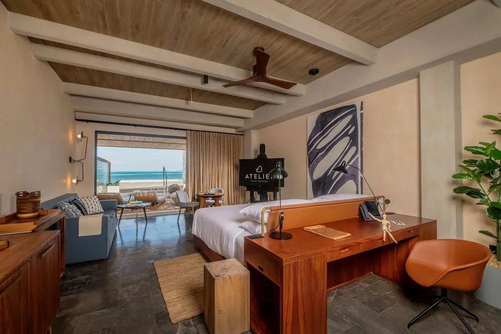 King-bed guest room with desk, sofa, terrace plunge pool, and ocean beyond at Atelier Playa Mujeres.