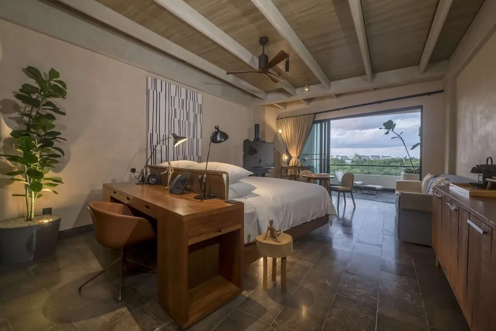 King-bed guest room with desk, terrace, and greenery view at Atelier Playa Mujeres.