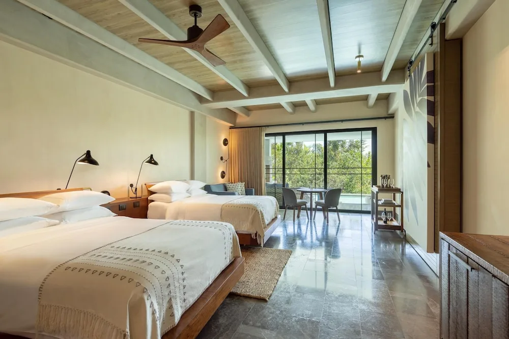 Two-bed guest room with balcony seating and leafy view at Atelier Playa Mujeres.