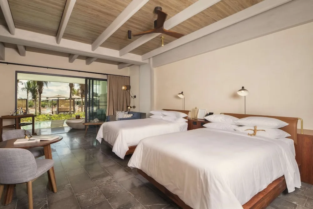 Guest room with two beds, seating area and terrace access at Atelier Playa Mujeres.