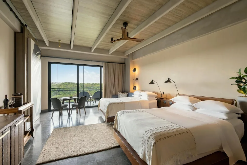 Two queen beds with balcony seating in a guest room at Atelier Playa Mujeres.