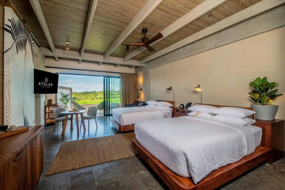Two-bed guest room with balcony doors, TV, and greenery view at Atelier Playa Mujeres.