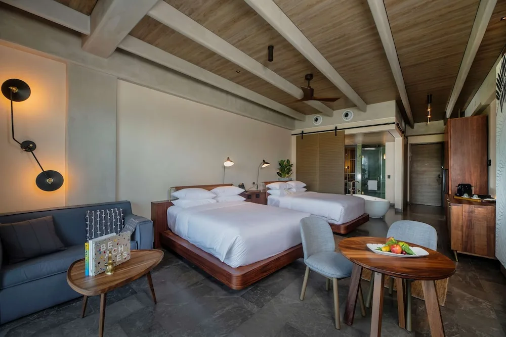 Two-bed guest room with sofa, dining table, and open bath area at Atelier Playa Mujeres.