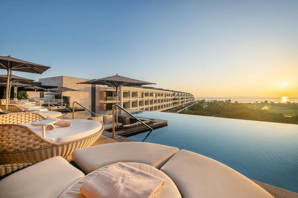 Infinity pool with cushioned loungers at sunset at Atelier Playa Mujeres.