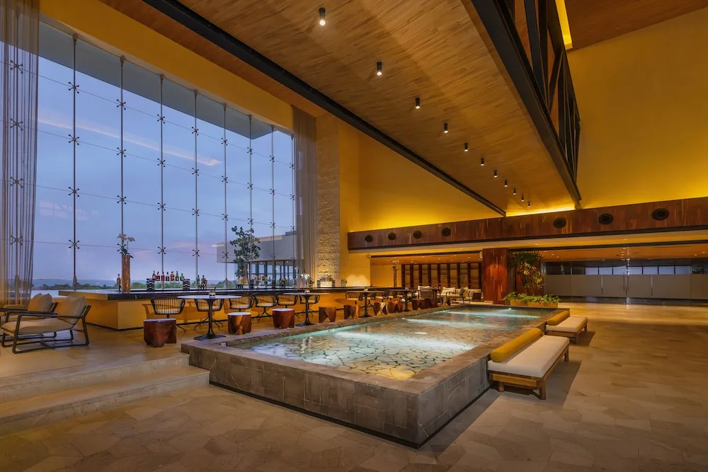 Lobby lounge at Atelier Playa Mujeres with a reflecting pool, bar seating, and tall windows.