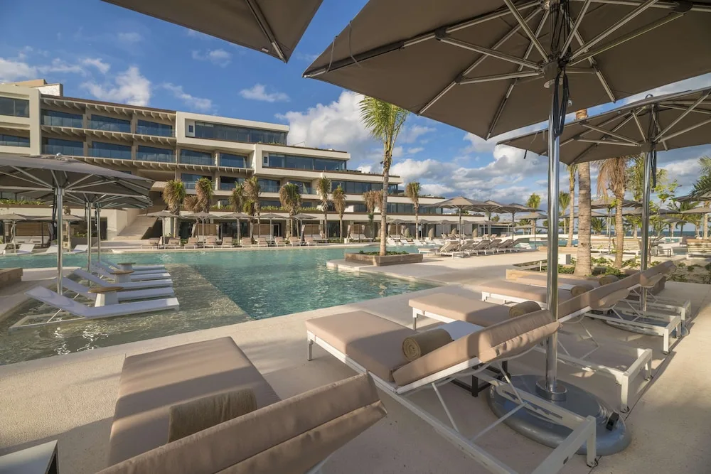 Pool deck with loungers, umbrellas and resort buildings at Atelier Playa Mujeres.