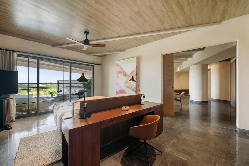 King bed suite with wood desk, balcony, and open hallway at Atelier Playa Mujeres.