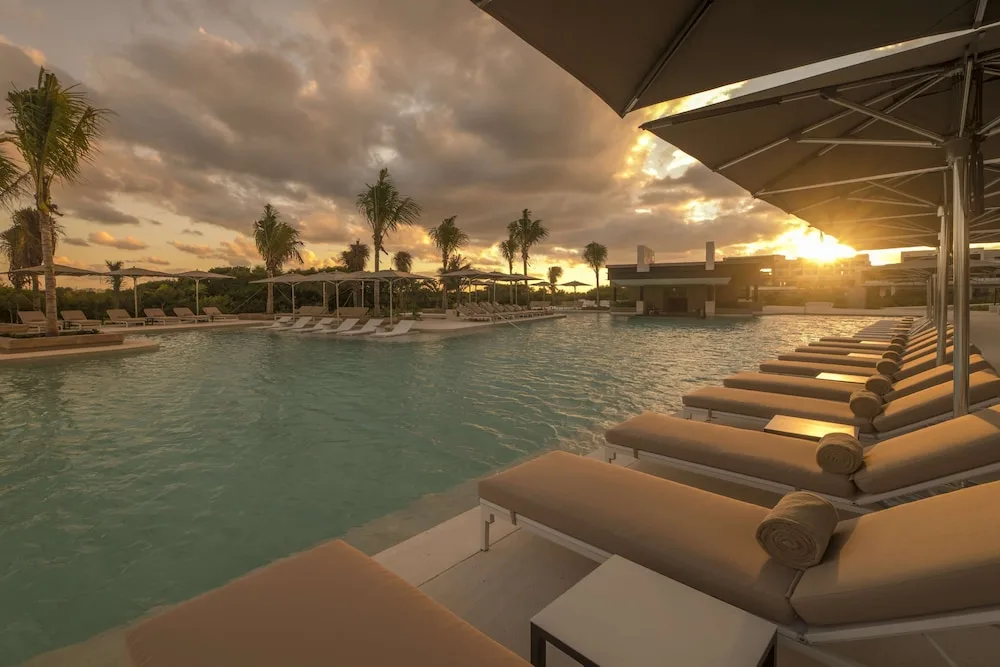 Sunset over the pool with loungers and umbrellas at Atelier Playa Mujeres.