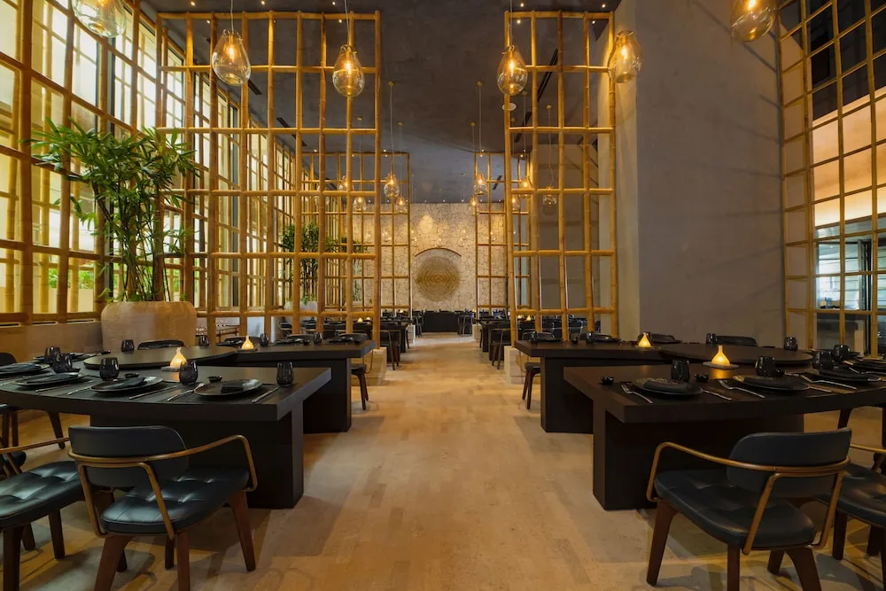 Modern dining room with dark tables, gold partitions and pendant lights at Atelier Playa Mujeres.