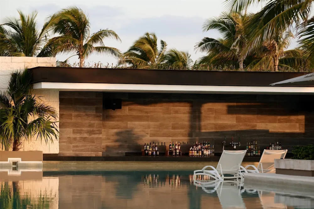 Pool bar counter with bottles, loungers, and palms at Atelier Playa Mujeres.
