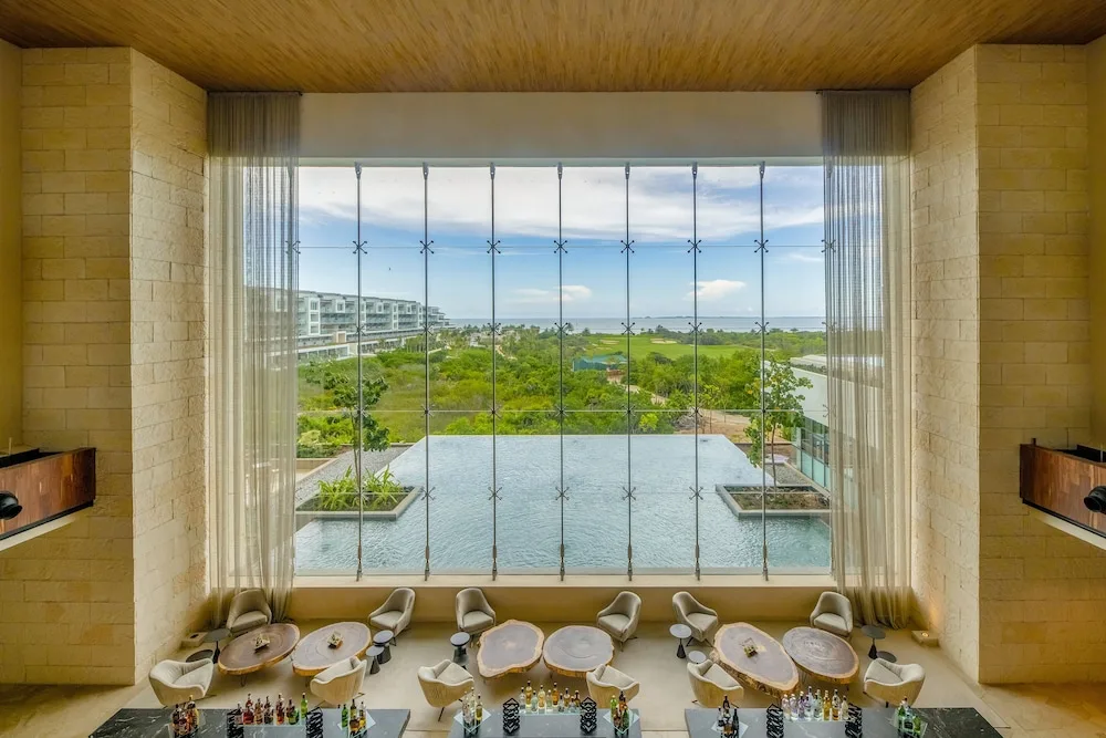 Upper lobby bar view at Atelier Playa Mujeres with tall windows, tables, and water beyond.