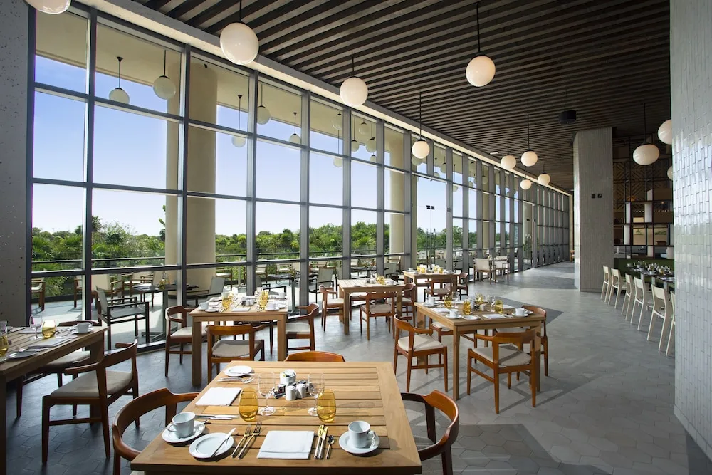 Sunlit restaurant tables beside tall windows at Atelier Playa Mujeres.
