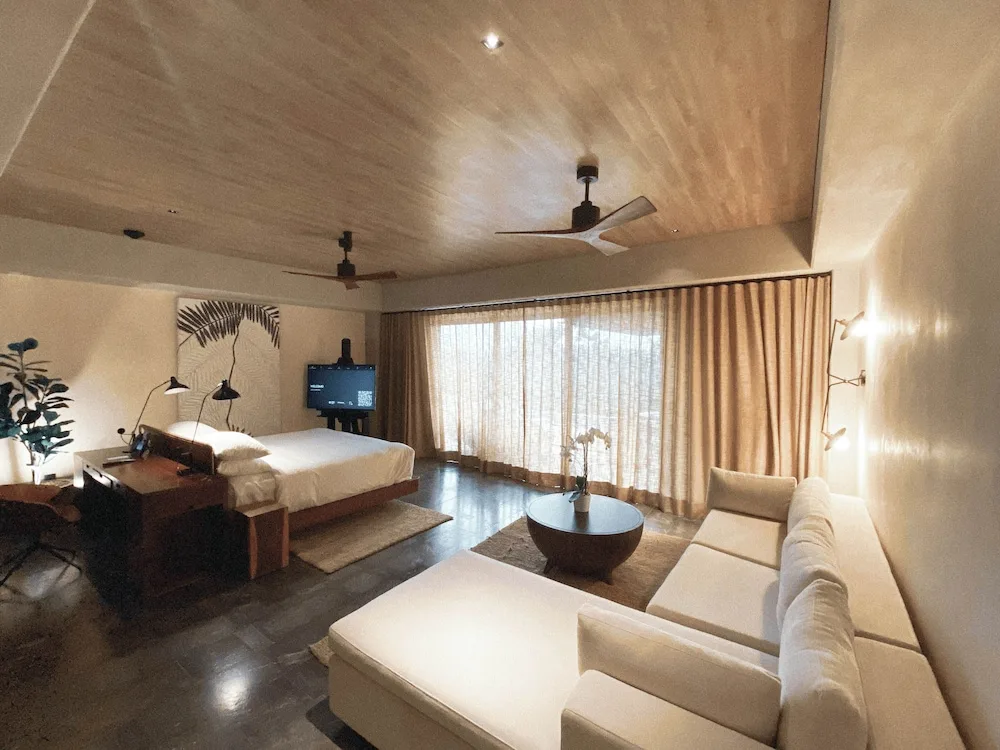 Inspira Corner Suite with bed, sofa and curtained windows at Atelier Playa Mujeres.