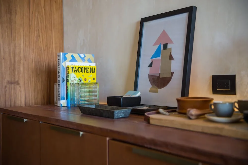 Junior Suite cabinet with books, framed art, cups, and tray at Atelier Playa Mujeres.