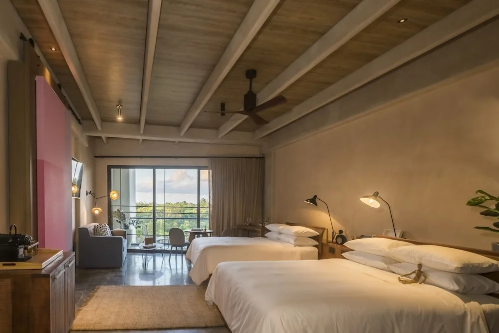 Junior Suite with two beds, balcony doors, sitting area, and wood ceiling at Atelier Playa Mujeres.