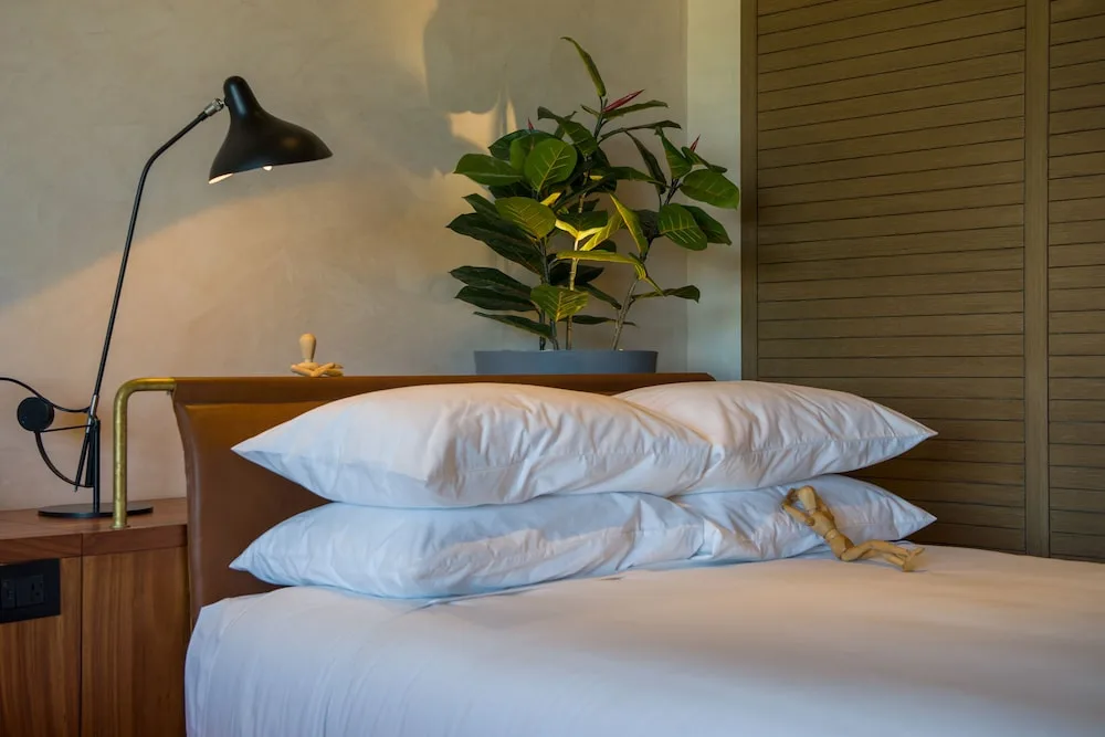 Close-up of the Junior Suite bed, pillows, lamp, and plant at Atelier Playa Mujeres.