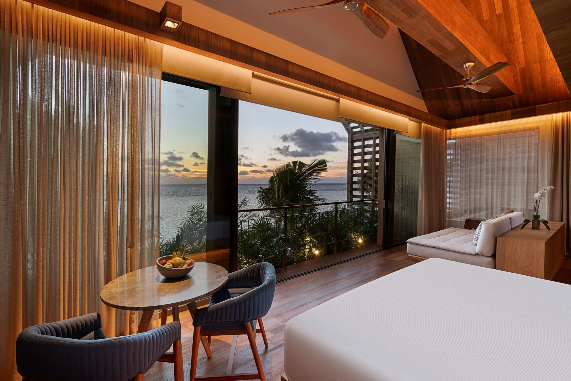Oceanfront Balcony Pool Suite bedroom at sunset with ocean-facing windows at Banyan Tree Mayakoba.