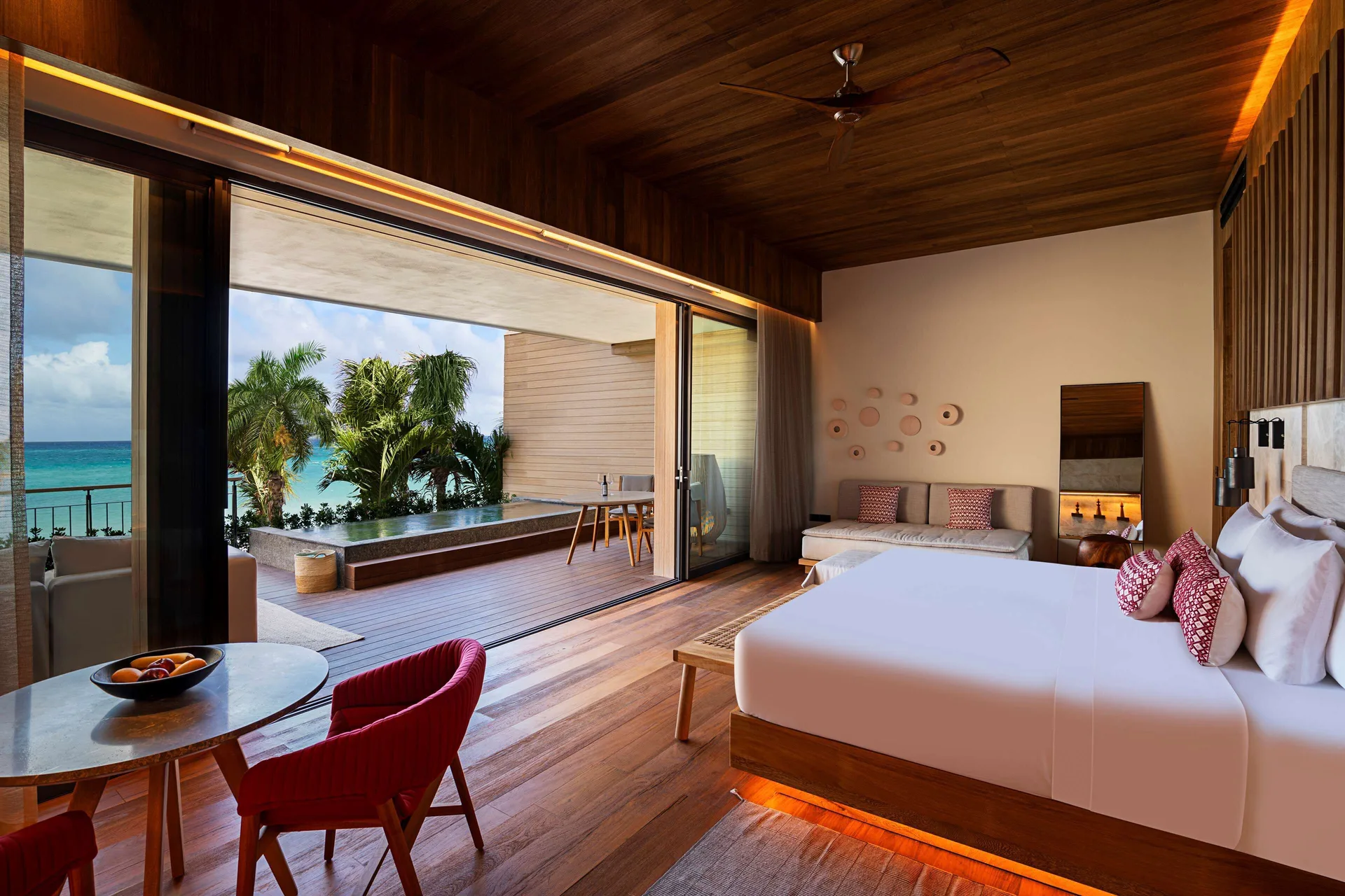 Oceanfront Veranda Pool Suite king bed beside glass doors and turquoise sea at Banyan Tree Mayakoba.