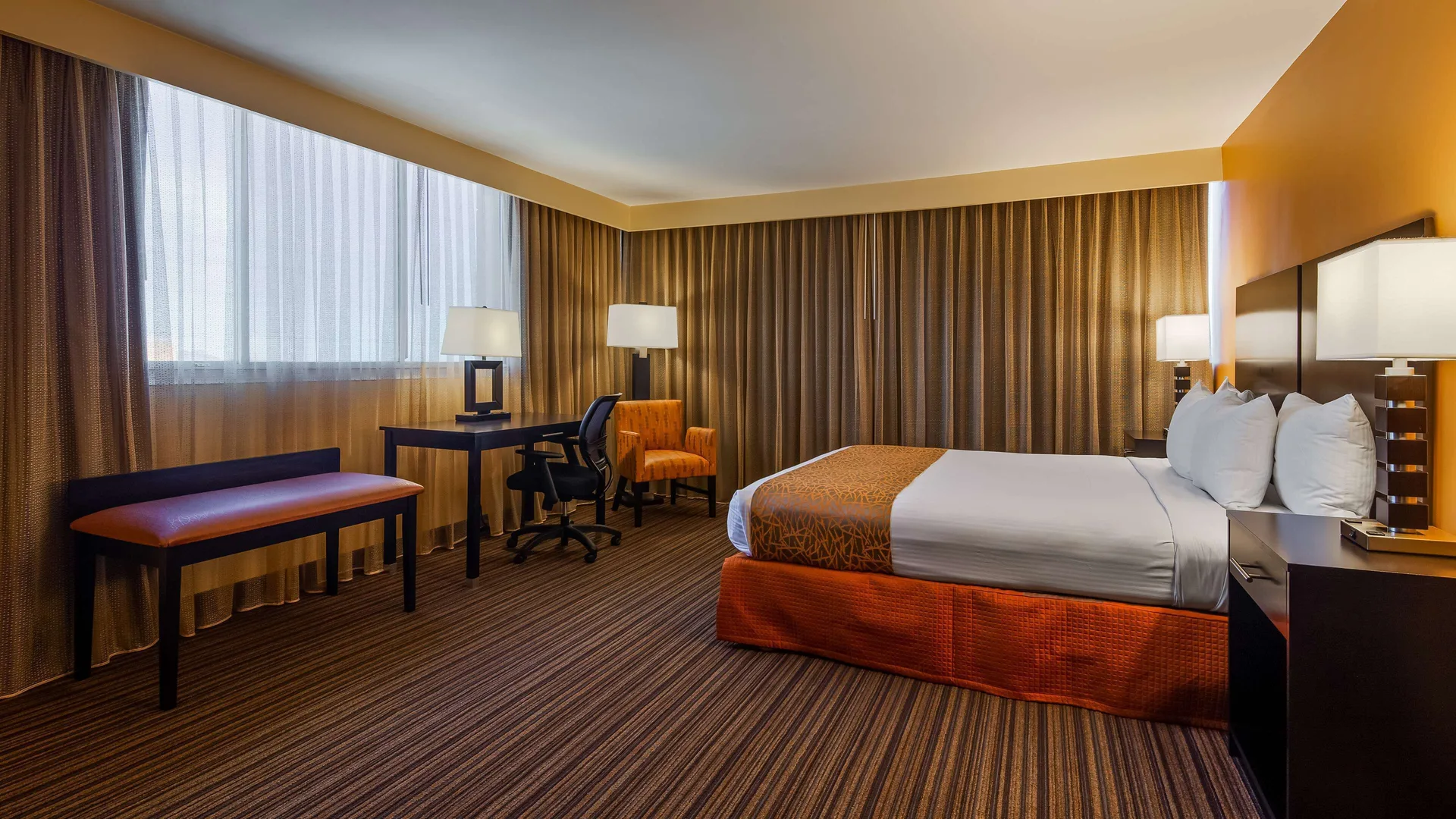 Standard room with king bed, desk, bench and curtained windows at Best Western The Plaza Hotel Honolulu Airport.