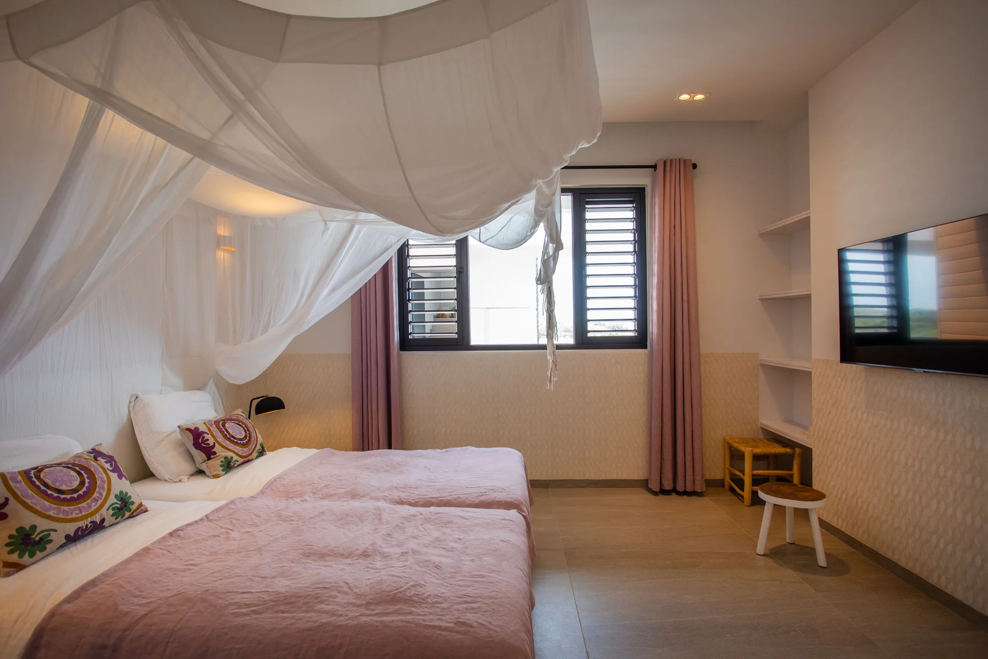 Twin beds with canopy netting and a wall-mounted TV at Blue Bay Curacao Golf & Beach Resort.