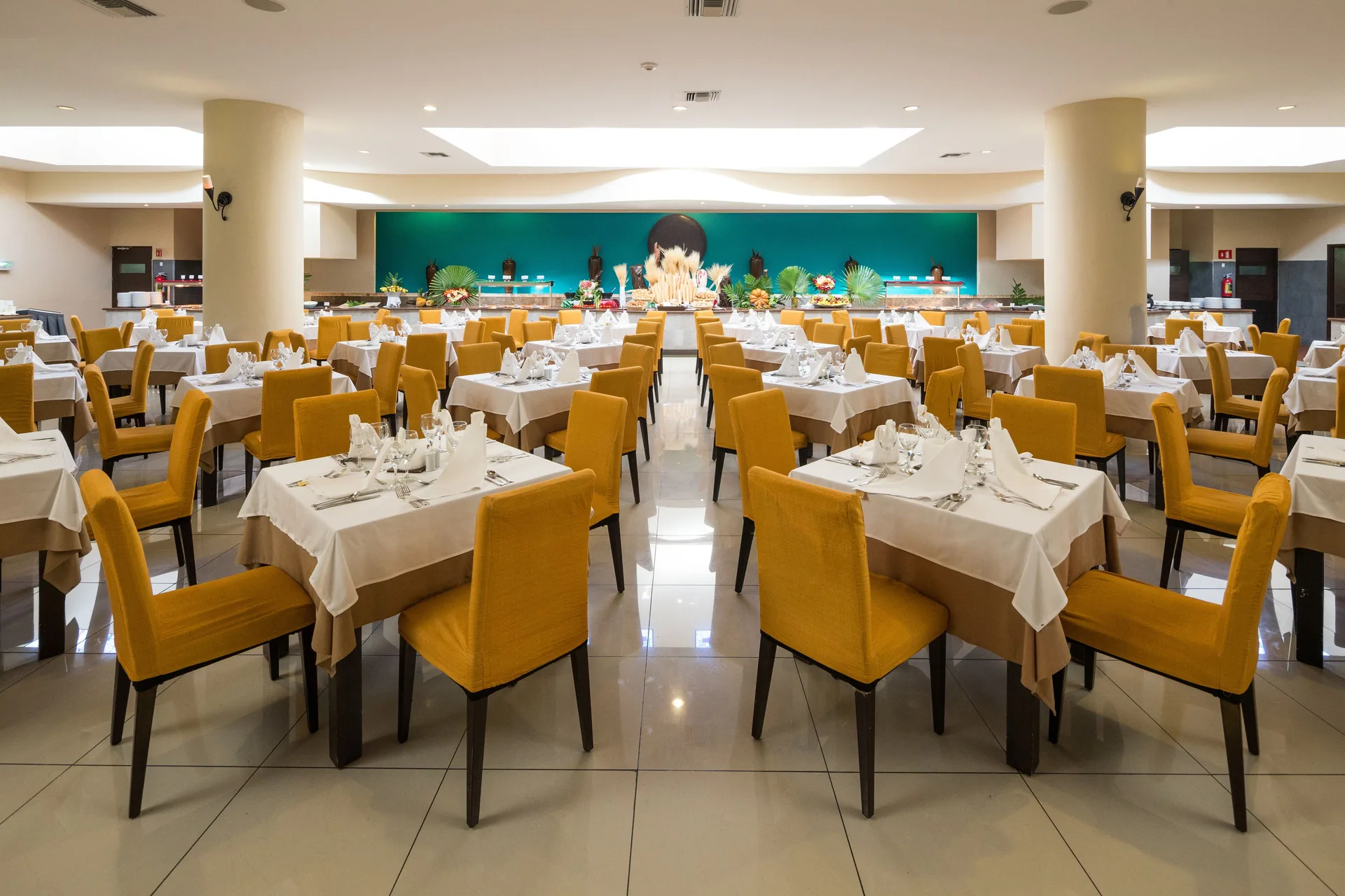 Buffet-style dining room with yellow chairs and white linens at BlueBay Grand Esmeralda.