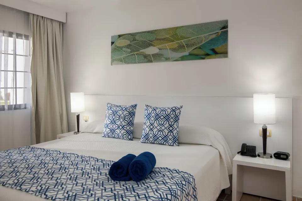 Standard Room bed with patterned pillows and blue towels at BlueBay Villas Doradas.