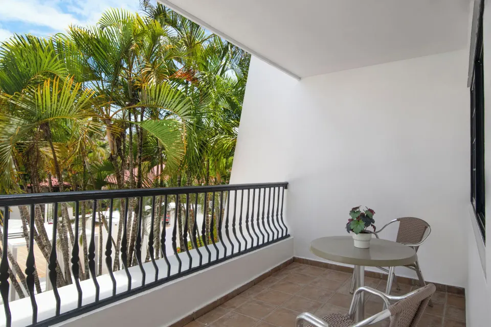 Superior Room balcony with table, chairs, and palm trees at BlueBay Villas Doradas.