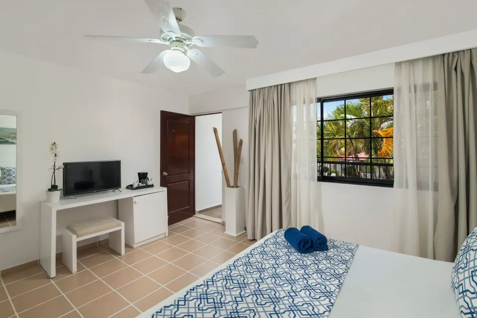 Superior Room king bed with TV, desk, ceiling fan, and window at BlueBay Villas Doradas.