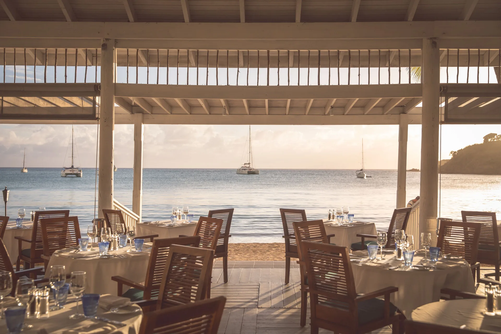 Open-air beachfront dining room with set tables and sailboats at Carlisle Bay.