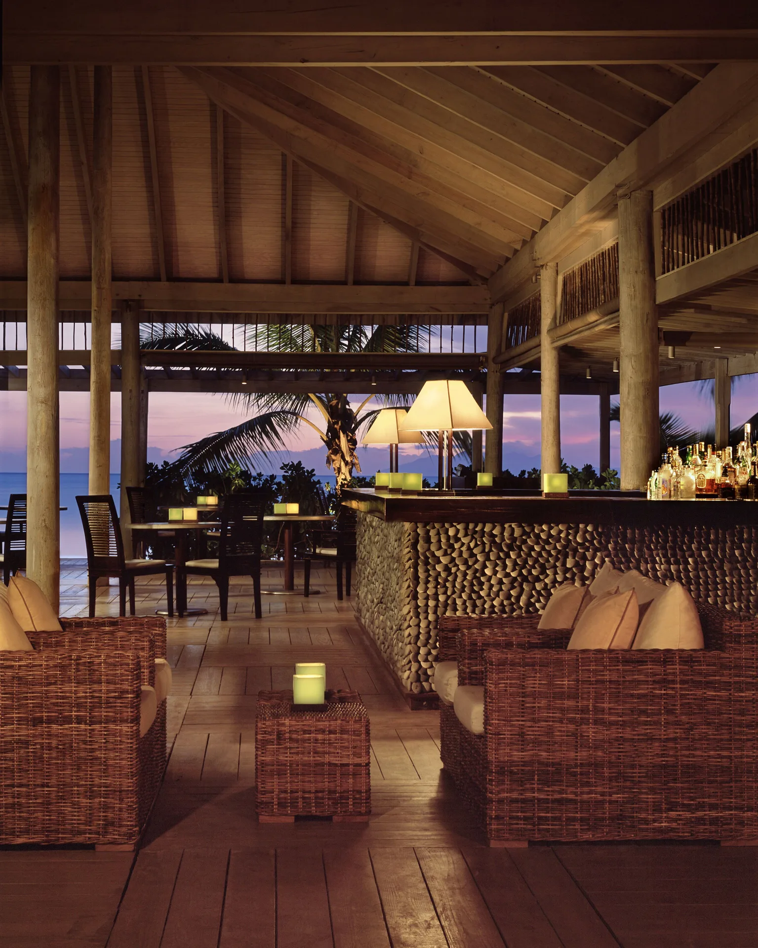Open-air bar with wicker seating, candles and an ocean backdrop at Carlisle Bay.