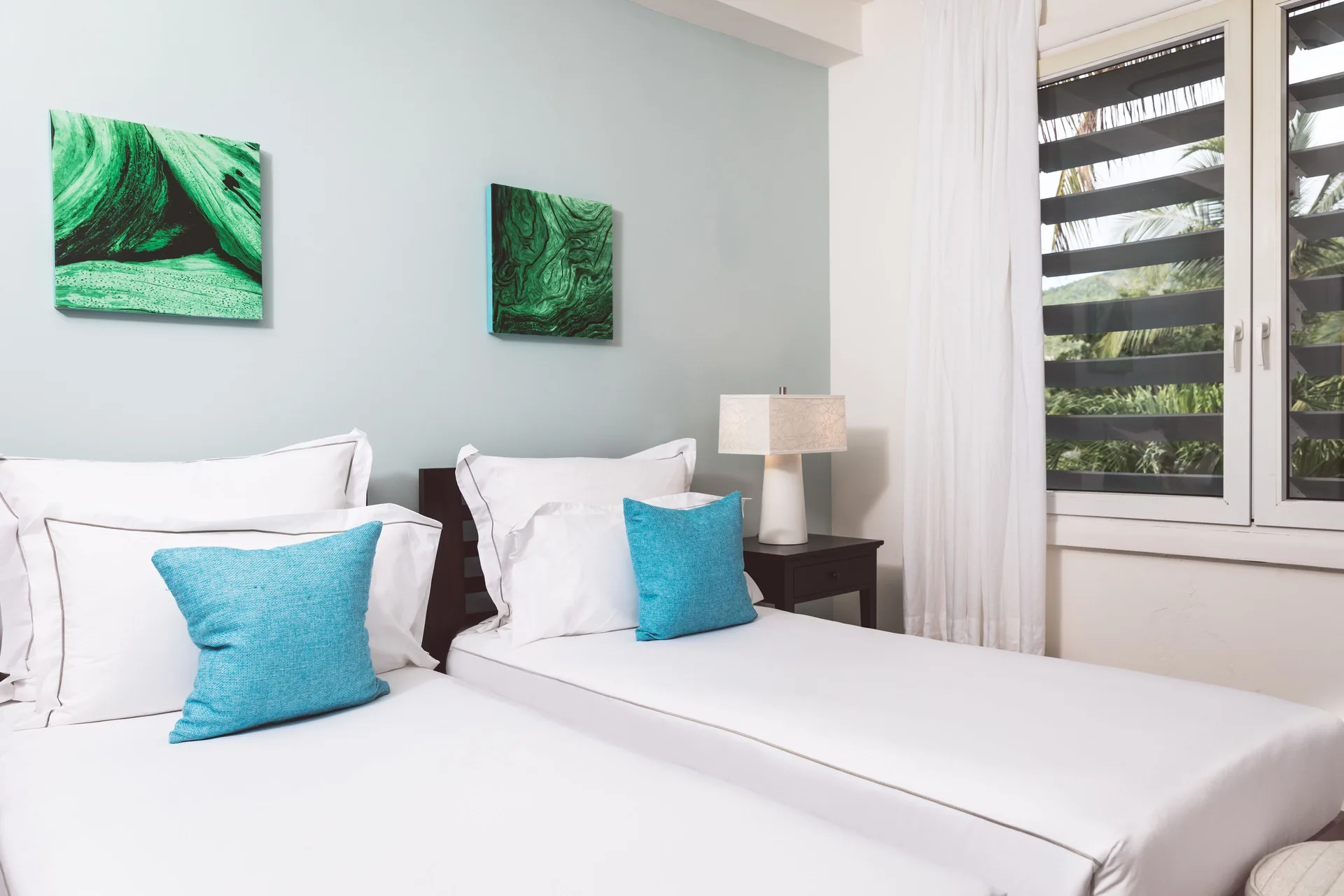 Twin beds in a beach balcony suite bedroom at Carlisle Bay with turquoise pillows and louvered windows.