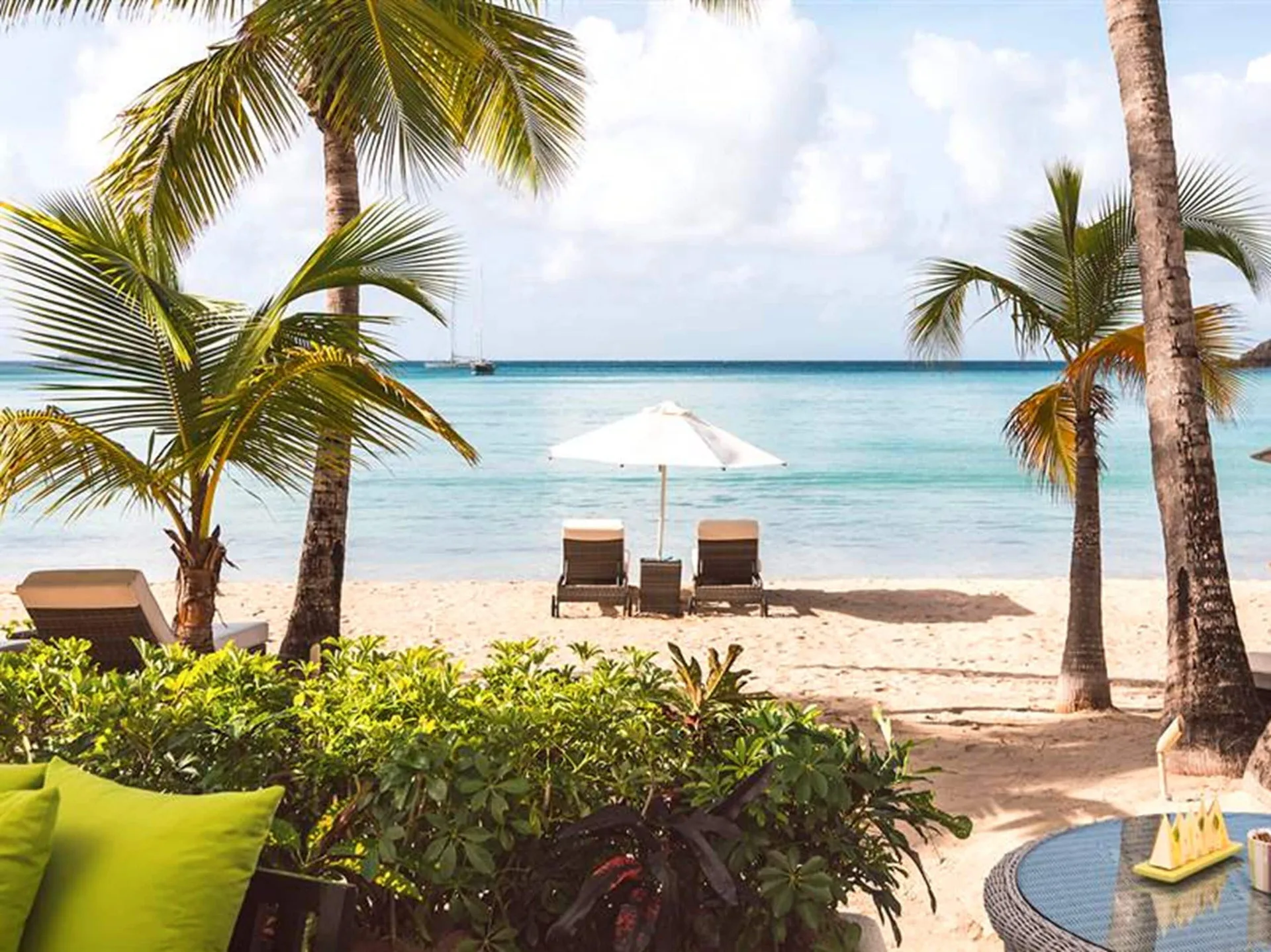 Beach view from a Terrace beach suite at Carlisle Bay with palms and loungers by the water.