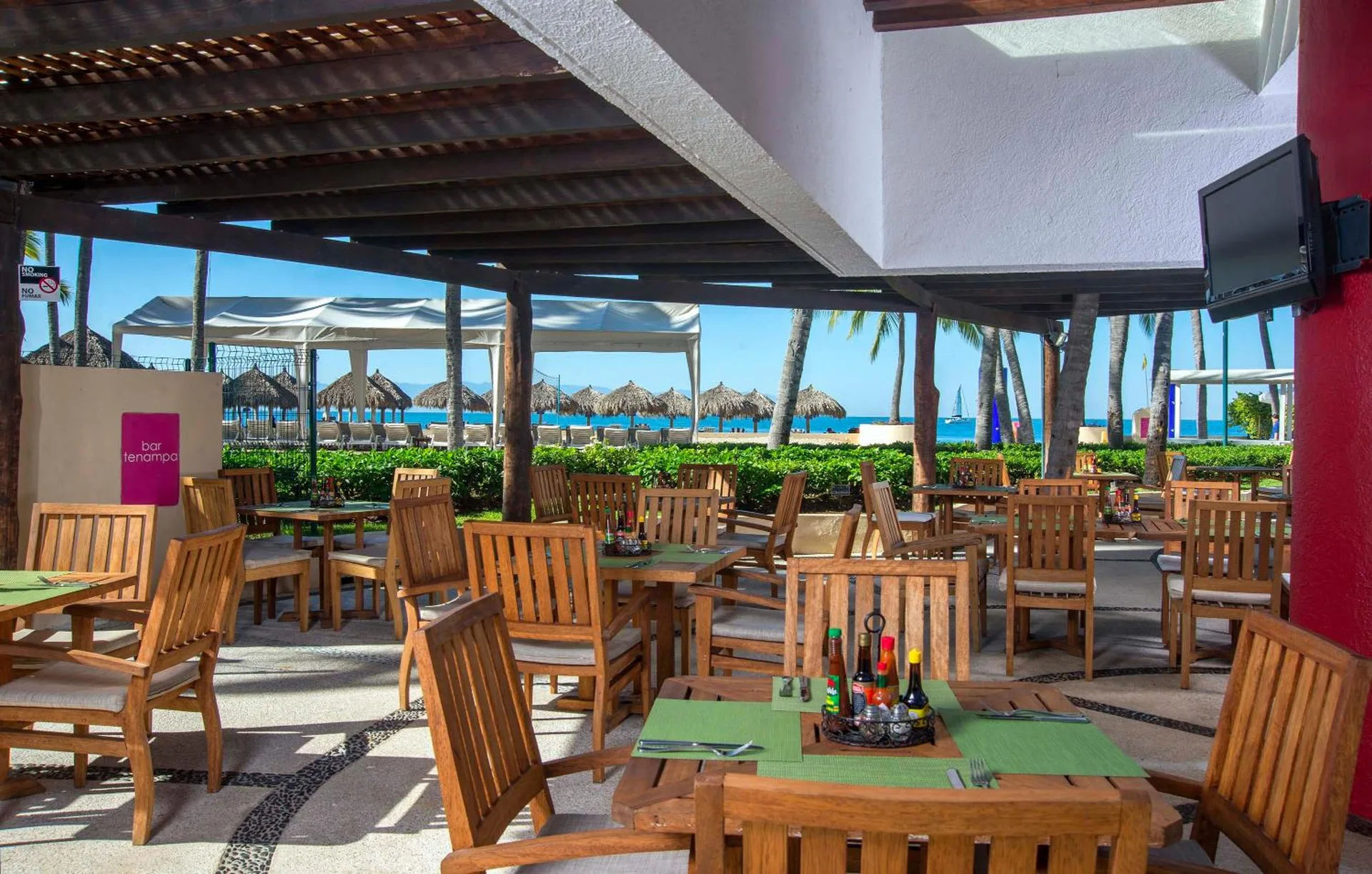 Tenampa Pool Bar terrace with wooden tables and ocean views at Club Regina Puerto Vallarta.