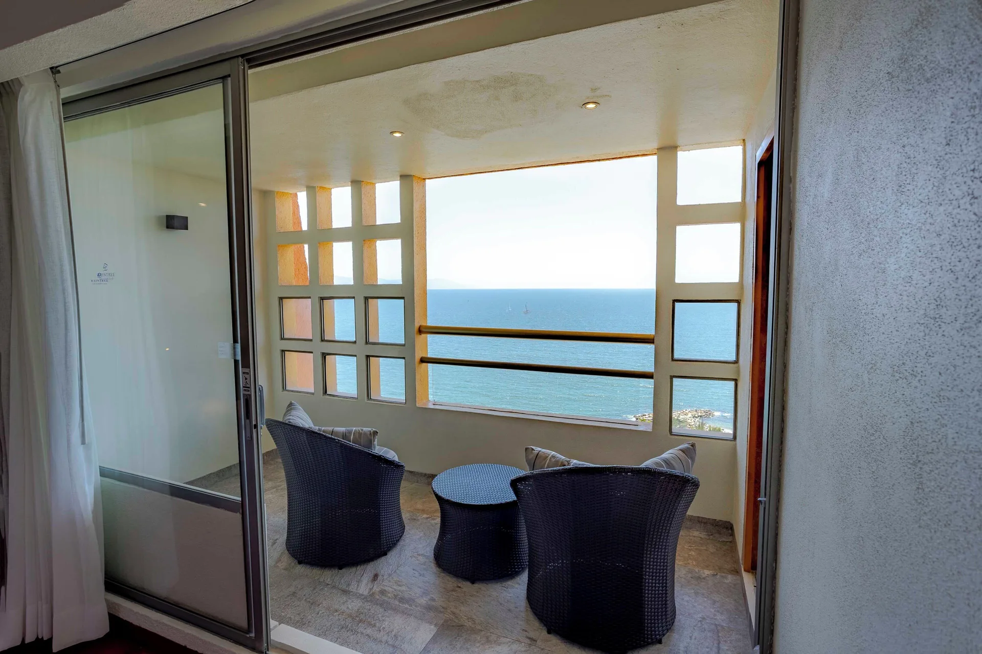 Suite balcony with two wicker chairs, round table, and ocean view at Club Regina Puerto Vallarta.